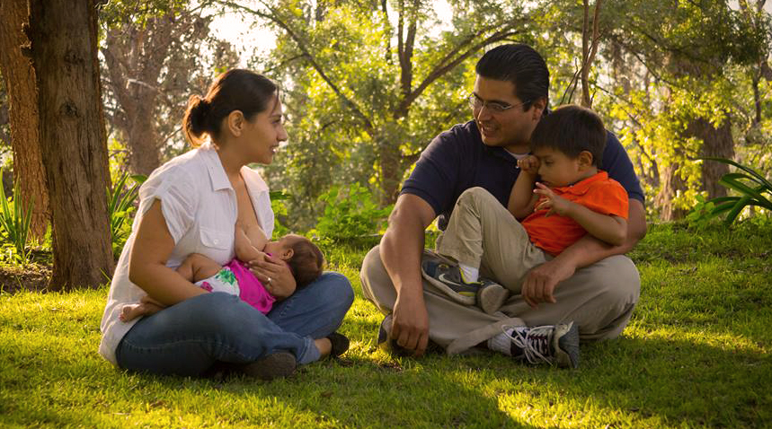 Familia en un jardín: una mamá amamanta a su bebé junto al papá y su hijo